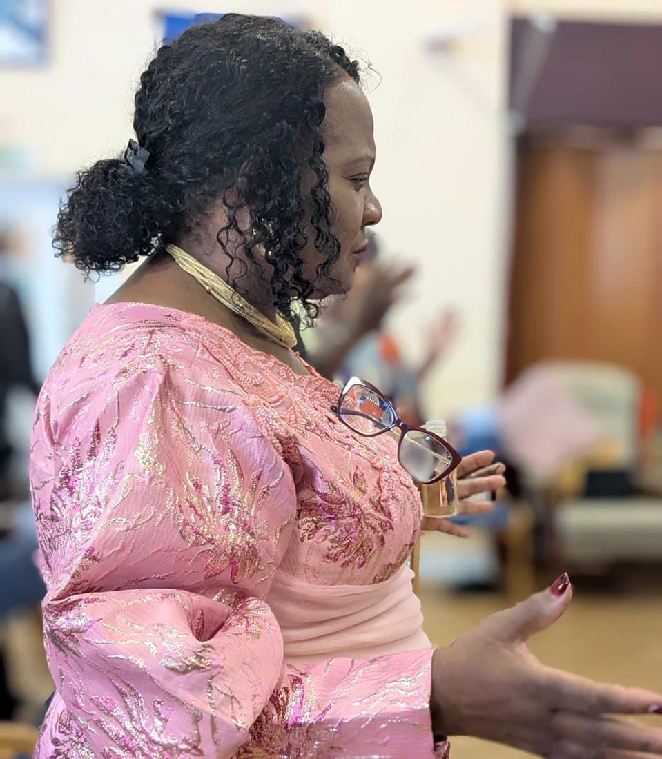 Pastor Catherine in pink, holding anointing oil as she ministers