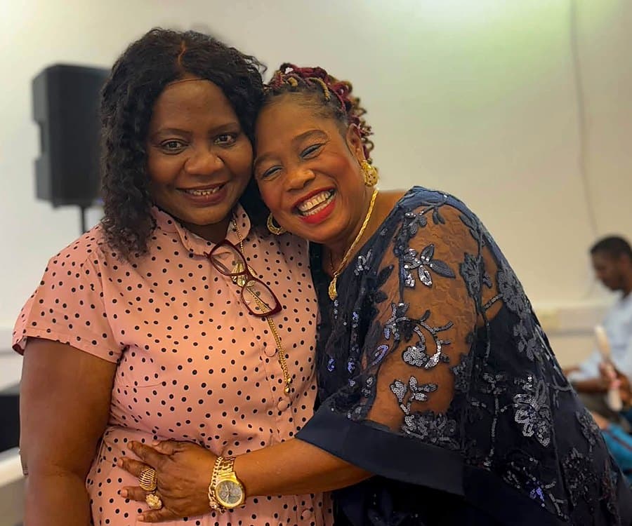 Pastor Catherine embracing a sister at a church gathering, both laughing